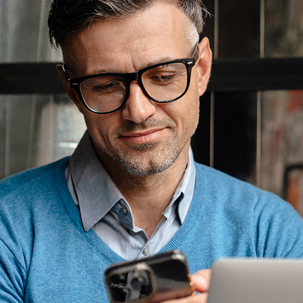 Man using his iPhone with a MacBook open