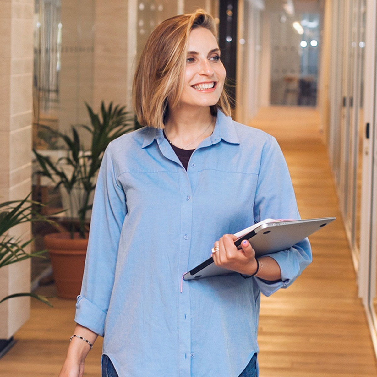 Woman walking down an office corridor carrying a MacBook