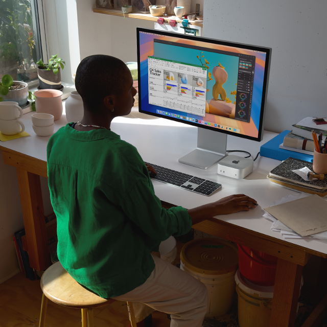 Person at a desk using a Mac mini and display to work in apps with colourful screen activity