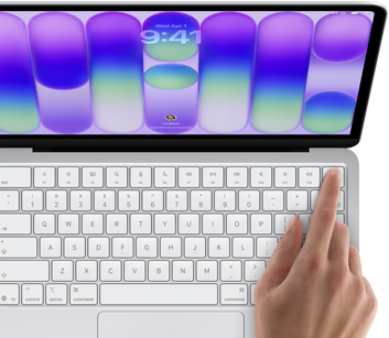 MacBook Neo, silver colour, showing login screen, person’s finger on Touch ID sensor in top-right corner of keyboard